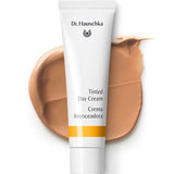 The Dr Hauschka Tinted Day Cream 30ml in a white tube rests on a beige cream smear, with branding and product name visible—ideal for achieving a natural glow with this tinted moisturiser.