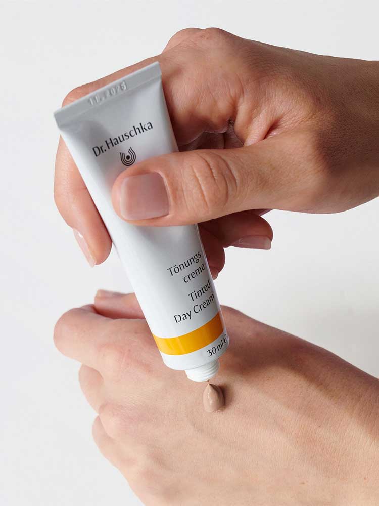A person squeezes a small amount of Dr Hauschka Tinted Day Cream 30ml onto the back of their hand for a natural, radiant glow.