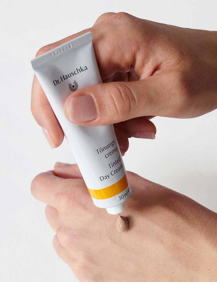 A person squeezes a small amount of Dr Hauschka Tinted Day Cream 30ml onto the back of their hand for a natural, radiant glow.