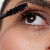 A close-up shows someone applying Dr Hauschka Volume Mascara 8ml to their upper lashes with a wand. Their eye is open, and their smooth, illuminated skin is visible.