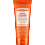 A bright orange tube of Dr Bronner's Organic Shaving Soap - Tea Tree 207ml stands upright against a white background, featuring white and orange text with product details and certifications.