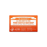 A 140g rectangular bar of Dr. Bronner's Pure-Castile Bar Soap in tea tree scent features an orange and white label with fair trade and organic details, plus product and brand information.