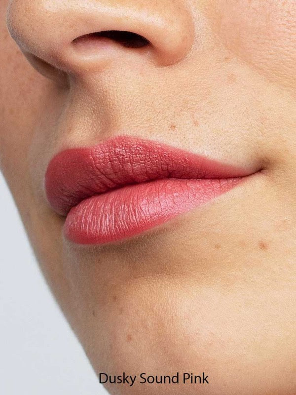 A close-up of lips wearing Antipodes Moisture Boost Natural Lipsticks 4g in matte dusky pink, with smooth skin visible. Infused with Avocado Oil for hydration. The text "Dusky Sound Pink" appears at the bottom of the image.