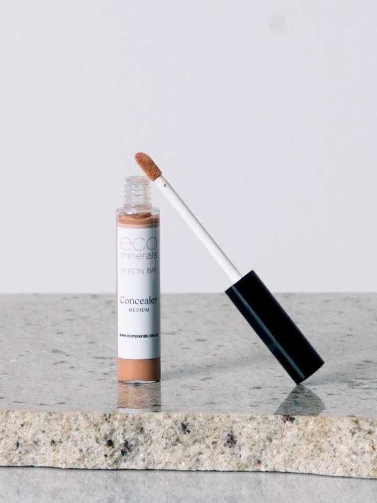 An open tube of Eco Minerals Mineral Concealer 5g, a vegan full-coverage product in Medium, with a wand applicator and simple white and brown packaging, rests on a granite surface.