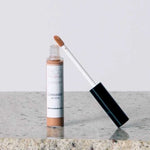 An open tube of Eco Minerals Mineral Concealer 5g, a vegan full-coverage product in Medium, with a wand applicator and simple white and brown packaging, rests on a granite surface.