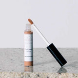 An open tube of Eco Minerals Mineral Concealer 5g, a vegan full-coverage product in Medium, with a wand applicator and simple white and brown packaging, rests on a granite surface.