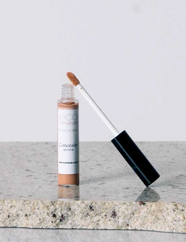 An open tube of Eco Minerals Mineral Concealer 5g, a vegan full-coverage product in Medium, with a wand applicator and simple white and brown packaging, rests on a granite surface.