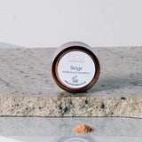 A small round container of Eco Minerals Perfection Dewy Mineral Foundation 5g sits on granite, with some loose powder spilled in front against a plain, neutral background.