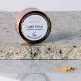 A 5g jar of Eco Minerals Flawless Matte Mineral Foundation sits on granite, with natural SPF25 and a touch of beige powder spilled nearby.