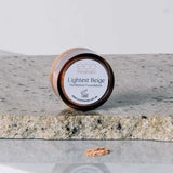 A small round container labeled Eco Minerals Perfection Dewy Mineral Foundation 5g sits on a stone surface with some loose powder in front, offering a natural dewy finish.