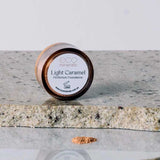 A small round container labeled “Eco Minerals Perfection Dewy Mineral Foundation 5g” rests on a stone surface with a mound of light brown powder in front, offering a dewy finish and enhancing natural radiance.