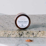 A small jar labeled Eco Minerals Perfection Dewy Mineral Foundation 5g sits on a gray stone surface, with a small pile of loose powder in front of it.