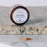 A small round container of Eco Minerals Flawless Matte Mineral Foundation 5g rests on a speckled stone surface, with loose powder in front showcasing its natural SPF25 protection and matte finish.