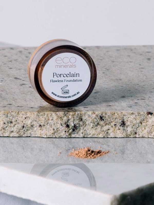 A small round container of Eco Minerals Flawless Matte Mineral Foundation 5g rests on a speckled stone surface, with loose powder in front showcasing its natural SPF25 protection and matte finish.