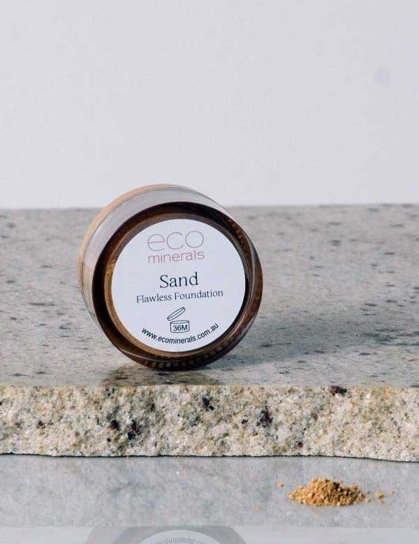 A 5g jar of Eco Minerals Flawless Matte Mineral Foundation rests on a stone surface, with some powder spilled beside it. The visible label shows the product name, website, and notes its natural SPF25 protection.