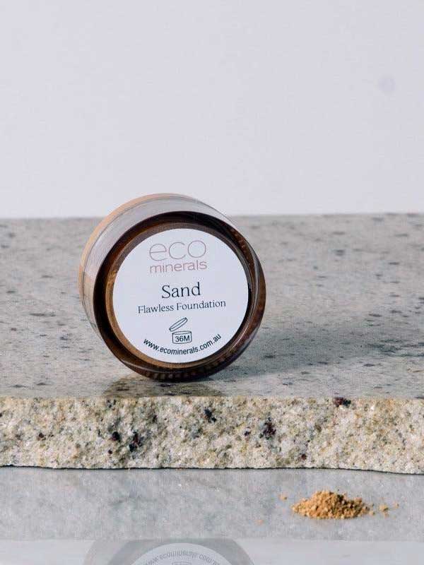 A 5g jar of Eco Minerals Flawless Matte Mineral Foundation rests on a stone surface, with some powder spilled beside it. The visible label shows the product name, website, and notes its natural SPF25 protection.