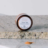 Eco Minerals Perfection Dewy Mineral Foundation 5g, in a round container on stone, is shown with loose powder in front—ideal for a dewy finish and natural SPF25 protection.