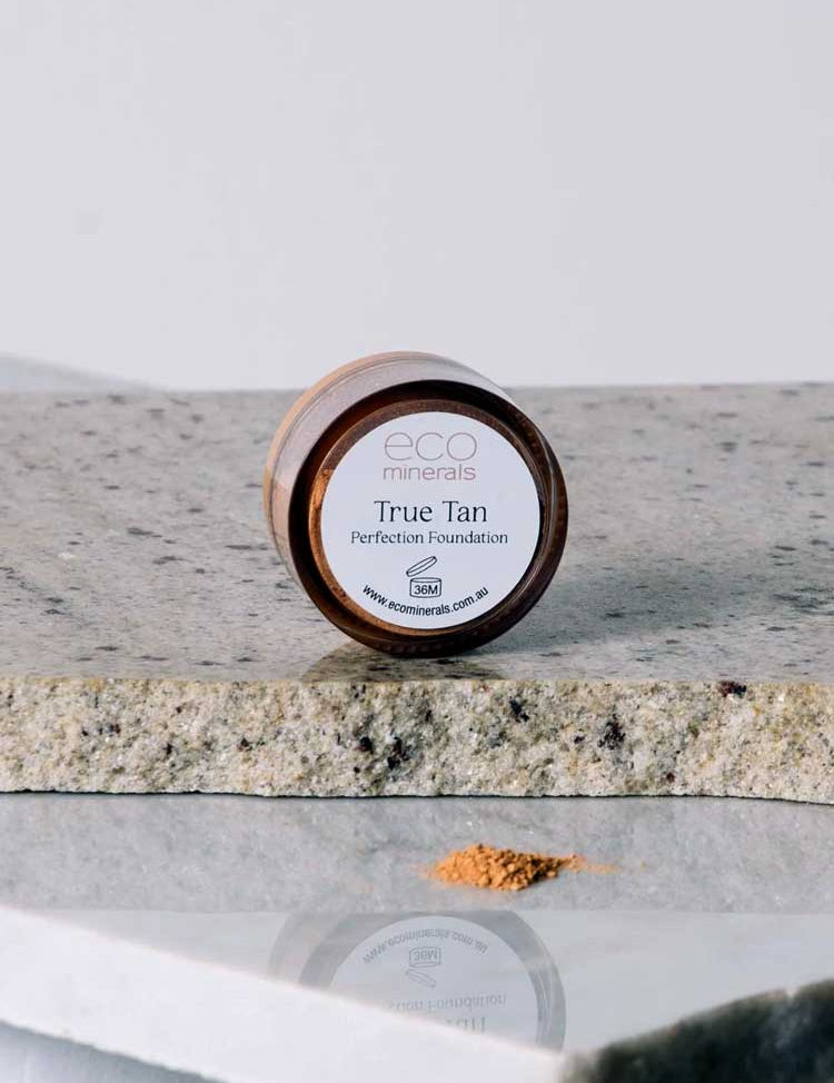 Eco Minerals Perfection Dewy Mineral Foundation 5g, in a round container on stone, is shown with loose powder in front—ideal for a dewy finish and natural SPF25 protection.