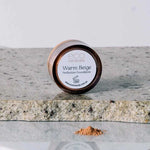 A 5g container of Eco Minerals Perfection Dewy Mineral Foundation rests on a stone surface, with some loose powder spilled beside it.