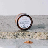 A 5g container of Eco Minerals Perfection Dewy Mineral Foundation rests on a stone surface, with some loose powder spilled beside it.