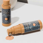 Two bottles of Eco Minerals Mineral BB Cream 32ml are shown—one upright, one lying with its cap off and dispensing light beige cream onto a white surface. Both display the “eco minerals BB cream, SPF 12” label.