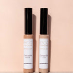 Two tubes of Eco Minerals Mineral Concealer 5g, one in Medium and one in Light, stand upright on a soft peach background with their black caps casting shadows.