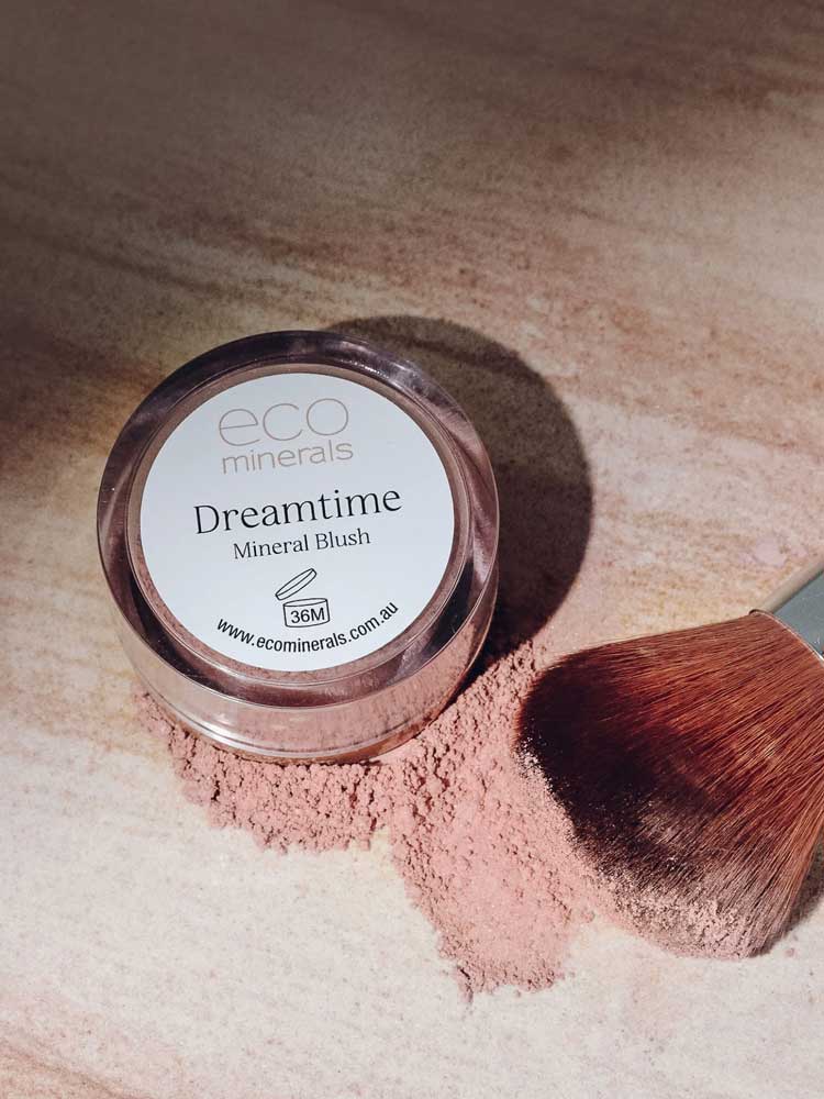 An Eco Minerals Mineral Blush - Dreamtime 4g sits on a light surface with blush powder spilled nearby and a makeup brush resting gently on the scattered vegan mineral blush.