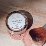 An Eco Minerals Mineral Blush - Dreamtime 4g sits on a light surface with blush powder spilled nearby and a makeup brush resting gently on the scattered vegan mineral blush.