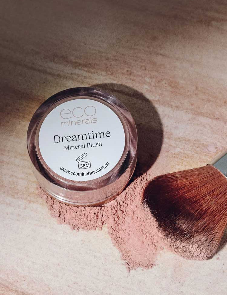 An Eco Minerals Mineral Blush - Dreamtime 4g sits on a light surface with blush powder spilled nearby and a makeup brush resting gently on the scattered vegan mineral blush.