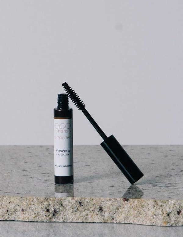 An open tube of Eco Minerals Natural Mascara 8g with a black wand sits on a granite countertop against a plain, light background.