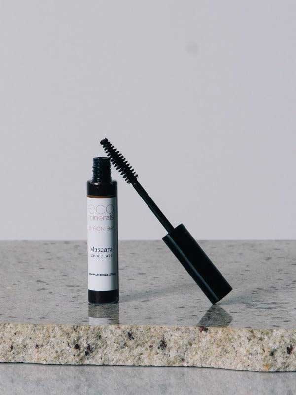 An open tube of Eco Minerals Natural Mascara 8g with a black wand sits on a granite countertop against a plain, light background.