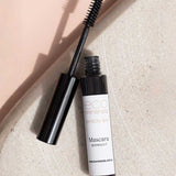 An open tube of Eco Minerals Natural Mascara 8g in the shade Midnight lies on a light textured surface, with the smudge-proof wand angled across the tube.