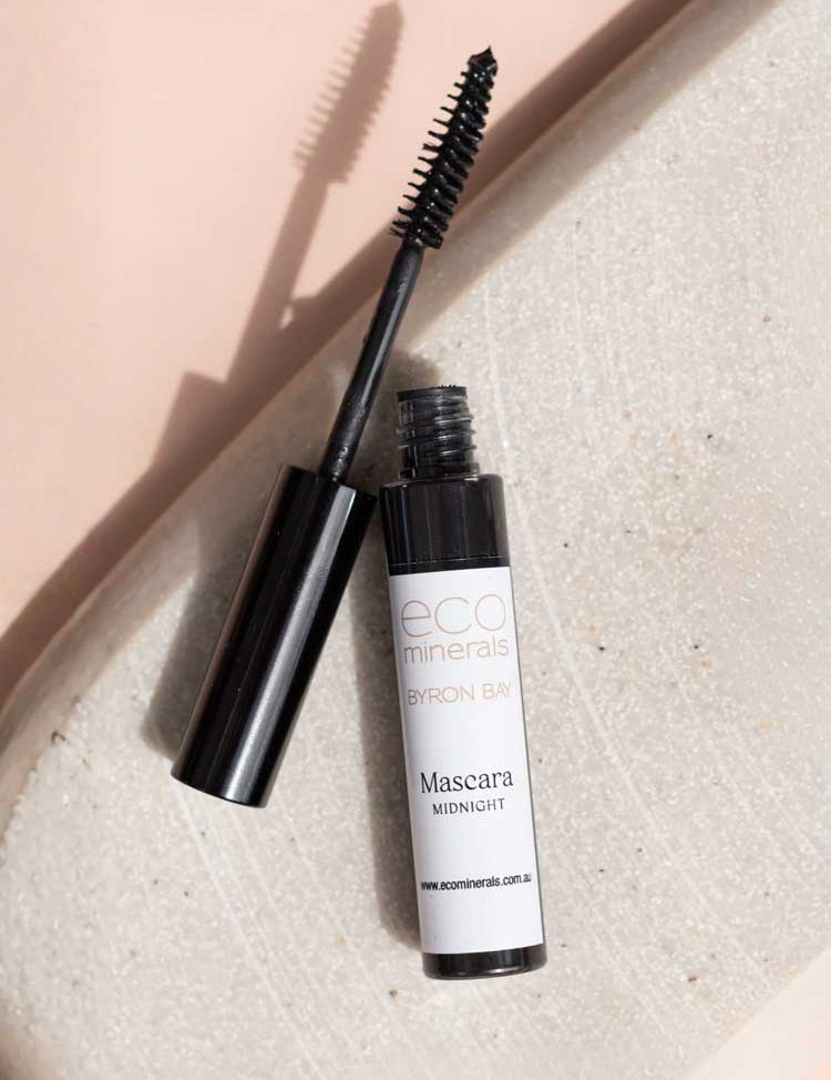 An open tube of Eco Minerals Natural Mascara 8g in the shade Midnight lies on a light textured surface, with the smudge-proof wand angled across the tube.