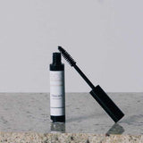 An Eco Minerals Natural Mascara 8g tube with the wand partially removed stands on a speckled stone surface against a plain light gray background.