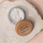 Open container of Eco Minerals White Light Illuminate 5g, a natural mineral highlighter with tan lid, resting on textured beige stone surface—ideal for anyone seeking an eco-friendly makeup option.