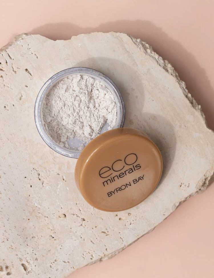 Open container of Eco Minerals White Light Illuminate 5g, a natural mineral highlighter with tan lid, resting on textured beige stone surface, ideal for anyone seeking an eco-friendly makeup option.