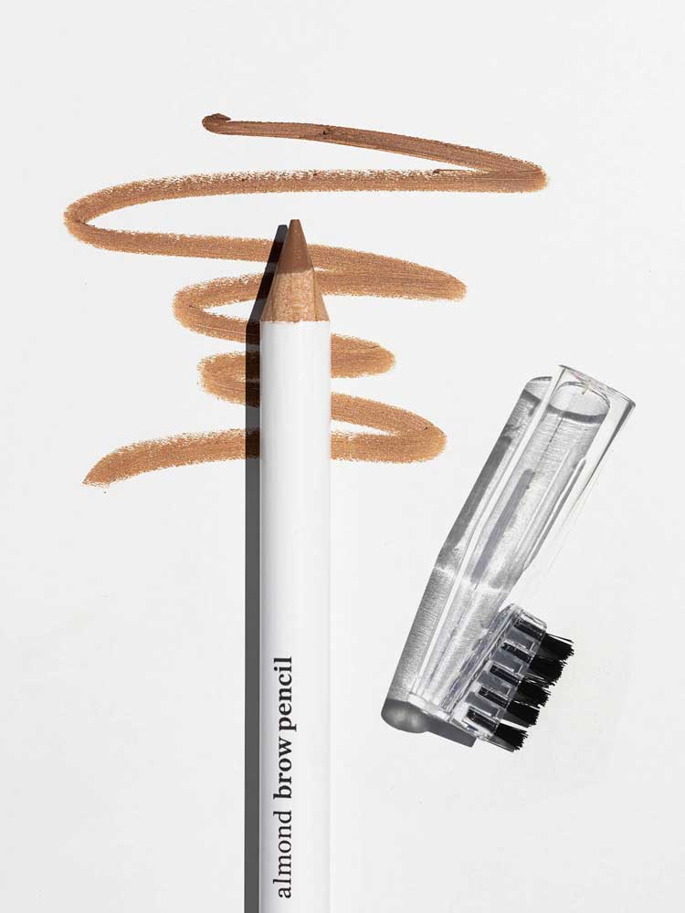 The Ere Perez Almond Brow Pencil 1.1g, a vegan brow pencil with a clear cap and attached brush, rests on a white surface; light brown strokes above display its natural effect. The label reads Ere Perez Almond Brow Pencil 1.1g.