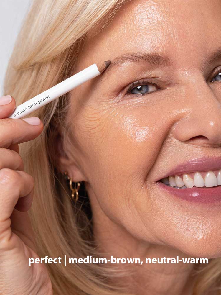 A smiling older woman with blonde hair applies Ere Perez Almond Brow Pencil 1.1g to her eyebrow. Text at the bottom reads: perfect | medium-brown, neutral-warm.