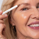 A smiling older woman with blonde hair applies Ere Perez Almond Brow Pencil 1.1g to her eyebrow. Text at the bottom reads: perfect | medium-brown, neutral-warm.