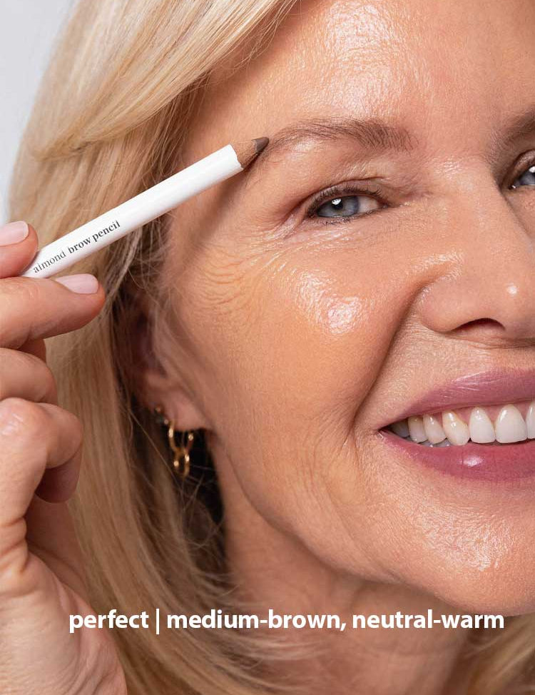 A smiling older woman with blonde hair applies Ere Perez Almond Brow Pencil 1.1g to her eyebrow. Text at the bottom reads: perfect | medium-brown, neutral-warm.