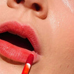 A close-up of a person applying Ere Perez Beetroot Cheek & Lip Tint - Joy 4.5ml with a wand, showing smooth skin and part of the face—ideal for achieving a natural, long-lasting lip stain.
