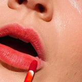 A close-up of a person applying Ere Perez Beetroot Cheek & Lip Tint - Joy 4.5ml with a wand, showing smooth skin and part of the face—ideal for achieving a natural, long-lasting lip stain.