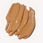 A close-up of Ere Perez Oat Milk Foundation 30ml, a creamy, medium-brown natural liquid foundation swatched in thick, smooth strokes on a white background.