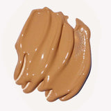 A close-up of Ere Perez Oat Milk Foundation 30ml, a creamy, medium-brown natural liquid foundation swatched in thick, smooth strokes on a white background.