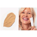 Swatch of beige Ere Perez Oat Milk Foundation 30ml on the left and a smiling older woman applying this natural medium coverage foundation in shade Chai (medium warm) to her cheek, holding the product tube. Text below: shade chai | medium warm | medium coverage.