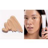 A swatch of Ere Perez Oat Milk Foundation 30ml in light-medium neutral shade “malt” appears on the left. On the right, a woman with radiant skin holds the natural liquid foundation tube by her face. Text below states: shade malt | light-medium neutral.