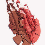 Crushed Ere Perez Rice Powder Blush & Bronzer - Brooklyn 9g in brown and red shades is smeared and scattered on a white background, with broken pieces and loose pigment mixed together.