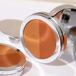 A close-up of the Ere Perez Rice Powder Bronzer - Tulum 9g compact, featuring two bronzer shades and "Ectetera" engraved on the powder, with two similar compacts in the background.