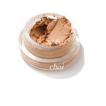The Ere Perez Arnica All-Cover Pot 5g in Chai is a creamy brown concealer in an open glass jar, set against a white background, that provides buildable coverage for a flawless finish.
