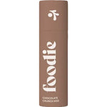 A brown cylindrical tube labeled "Foodie Chocolate Crunch Kiss Lip Balm 10g" stands upright against a white background—this chocolate lip balm features plastic-free packaging.